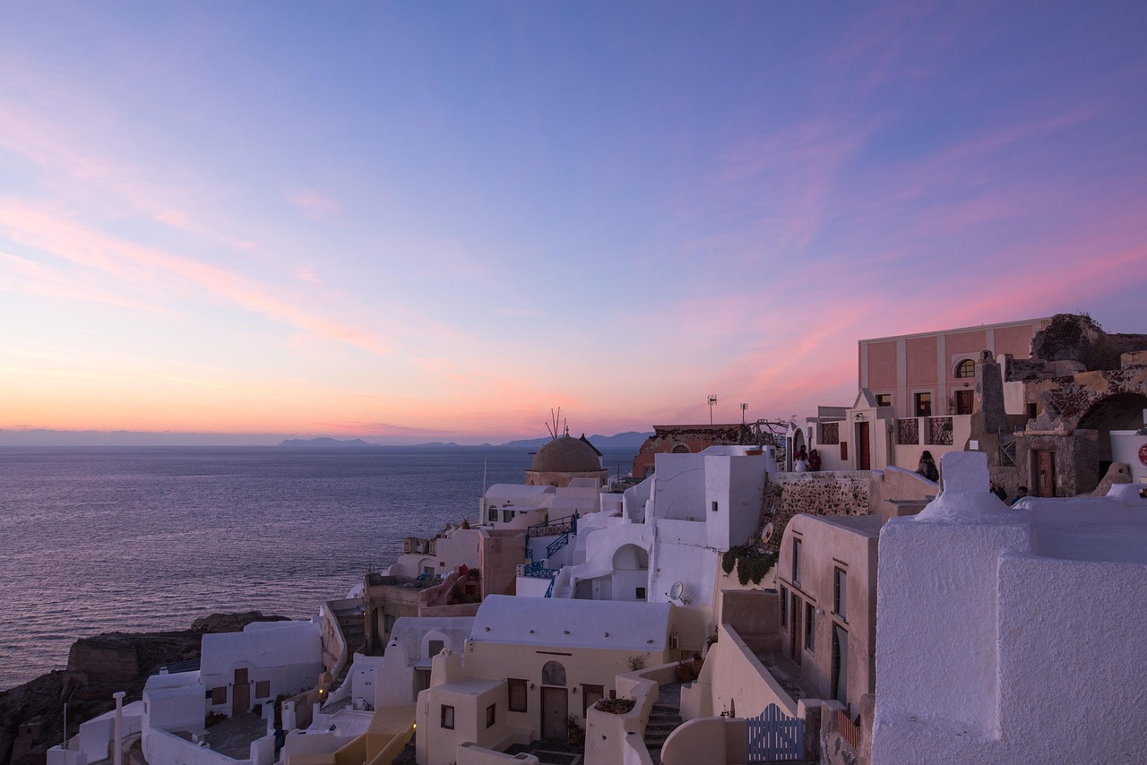 The whitewashed village of Oia in Santorini glowing under a pastel sunset